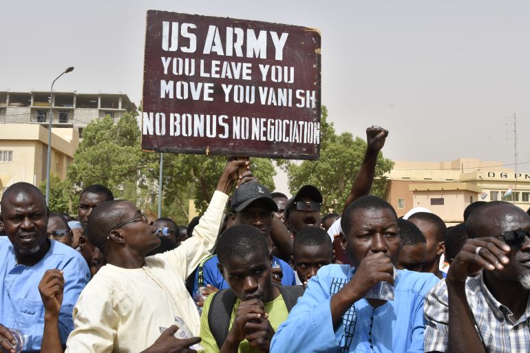 Protesters react as a man holds up a sign demanding that soldiers from the United States Army leave Niger