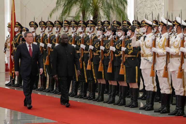 Manasseh Sogavare and China's Premier Li Qiang walking past an honour guard in Beijing. The giards are on the right. The two men are walking on a red carpet and Sogavare is nearest the guards.
