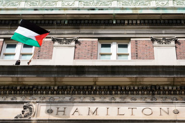 A pro-Palestinian student protester waves a Palestinian flag from a balcony of Hamilton Hall