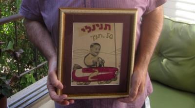 Grunbaum holds a picture of an advertisement featuring him as an infant to promote his parents' baby clothes business [Jonathan Cook/Al Jazeera] 