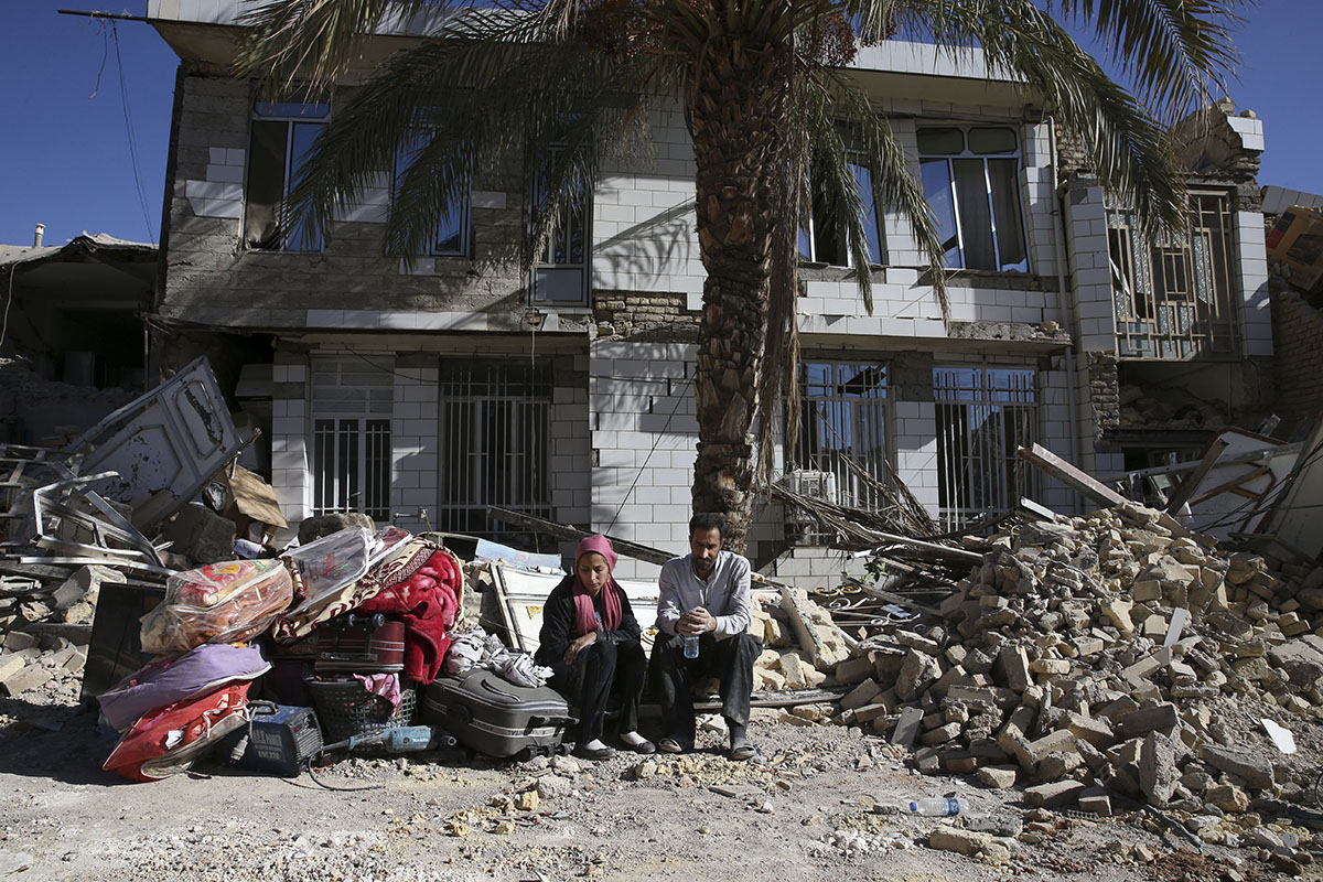 Los sobrevivientes se sientan frente a una casa destruida en el sitio del terremoto en Sarpol-e-Zahab en el oeste de Irán.  [Vahid Salemi / Foto AP]