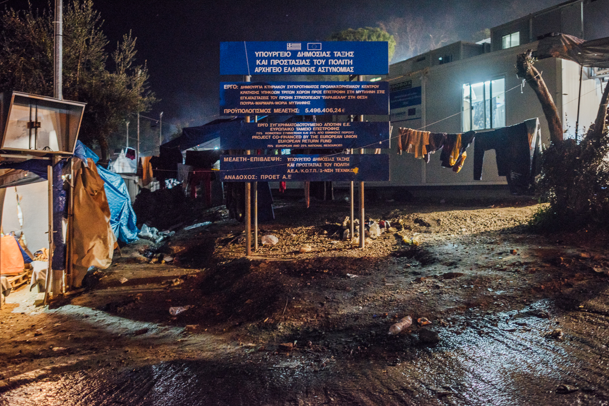 A sign reads that the EU and the Greek government spent more than 5.4 million euro ($6.6m) on Moria camp. [Kevin McElvaney/Al Jazeera]