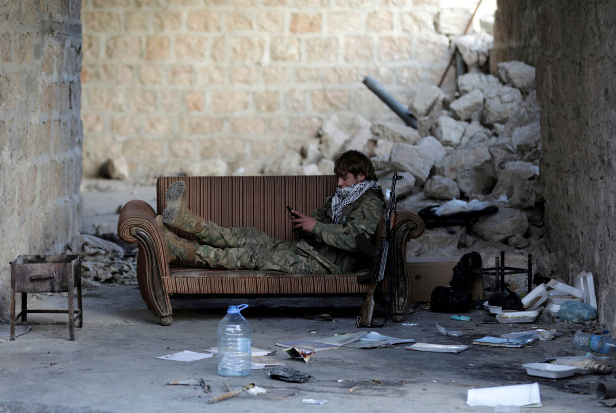 A Turkey-backed Free Syrian Army fighter holds a mobile phone in the town of Tadef in Aleppo Governorate, Syria. [Khalil Ashawi/Reuters]