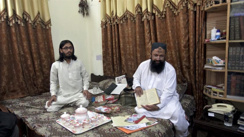 Malik Ishaq (R) sits on a bed with his son Malik Usman during an interview with Reuters at his home in Rahim Yar Khan [Reuters]