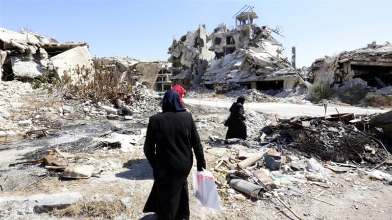 People walk between rubble in the city of Homs in Syria [EPA]