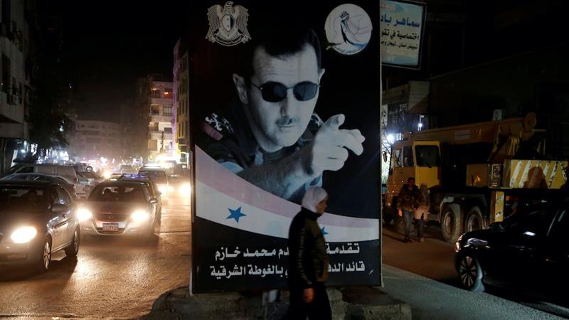 A woman walks past a poster of Syria's President Bashar al-Assad in Damascus [File: Yamam al-Shaar/Reuters]