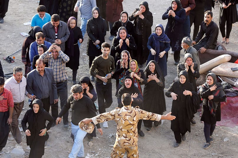 Un soldado hace un gesto mientras las víctimas iraníes del terremoto lloran e intentan acercarse al cuerpo de un pariente en torno a los restos de su hogar en la ciudad de Pole-Zahab.  [Abedin Taherkenareh / EFE / EPA]