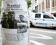 A police car drives past a poster accusing police of murder  