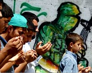 Palestinian boys pray in front of Hamas graffiti in Gaza city 