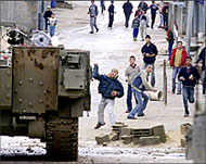 Palestinian youth throw stones at an Israeli armoured carrier