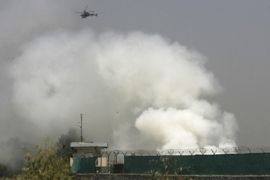 A NATO helicopter flies above the scene of a raid as smoke rises from a base in Jalalabad
