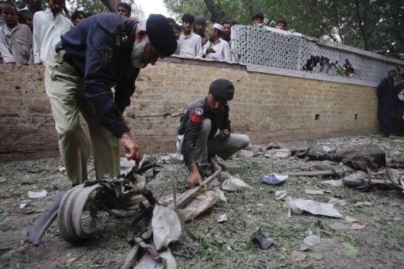 Policemen survey the site of a bomb attack outside a shrine in Peshawar