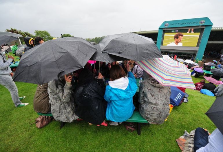 Tennis fans shelter under umbrellas as t