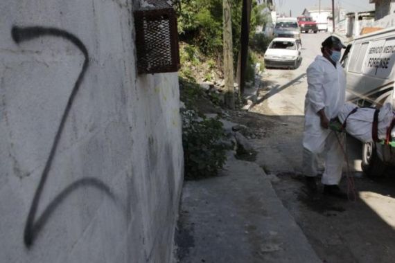 Forensic technicians remove a body from a crime scene near a wall spray painted with the