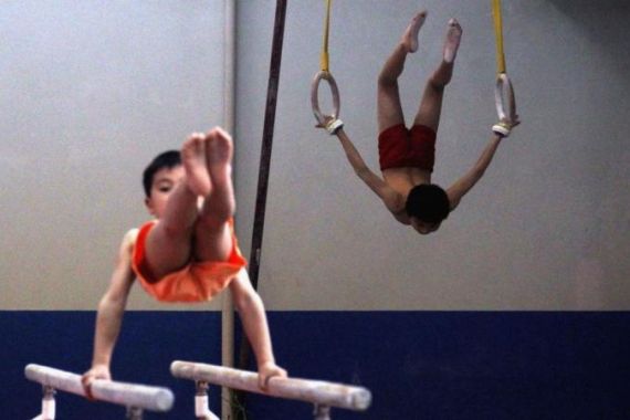 A young gymnast practices on gymnastic rings as another trains on the parallel bars during a gymnastics class for children aged between seven and ten at the Shichahai Sports School in Beijing