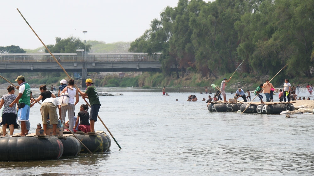 Hundreds of people cross the border between Mexico and Guatemala over the Suchiate river every day. In the background is the bridge and legal pass that links both countries [Amparo Rodriguez/Al Jazeera]