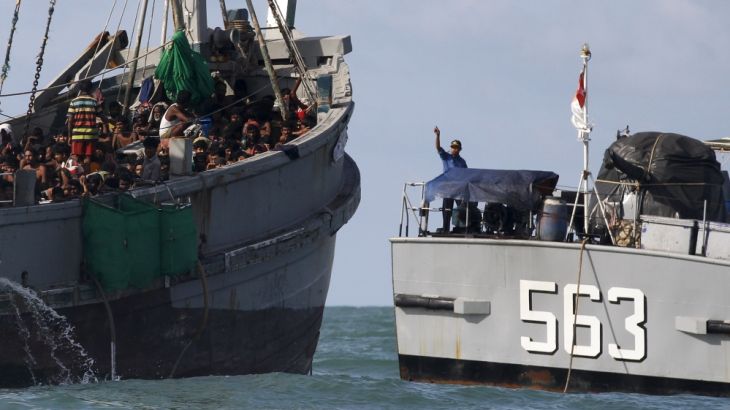 A Myanmar military officer gestures from a navy ship towards a boat packed with migrants, off Leik Island in the Andaman Sea