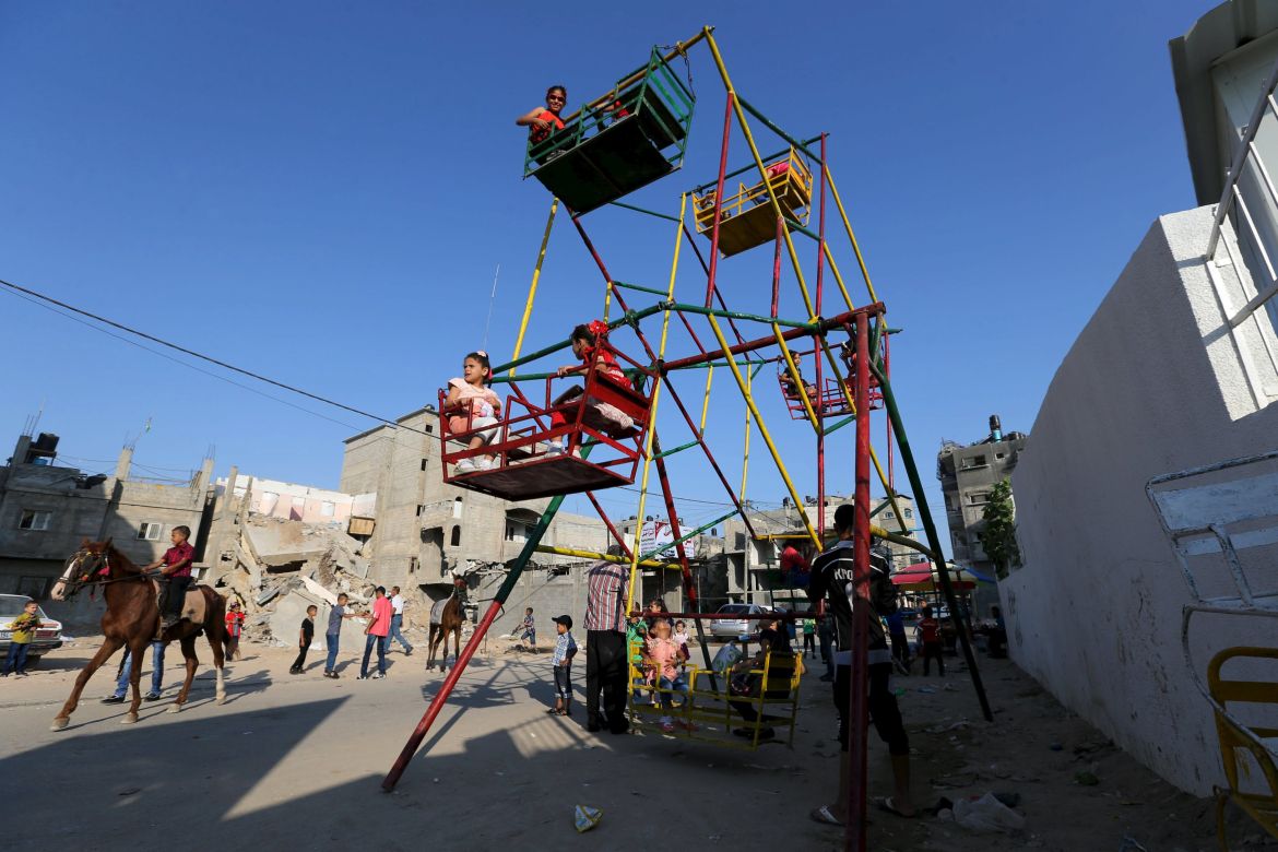 Palestinian children enjoy a ride on a ferris wheel, near the ruins of houses