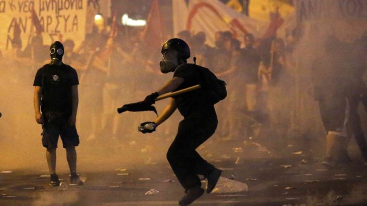 A masked youth hurls a projectile at riot police during clashes in Athens