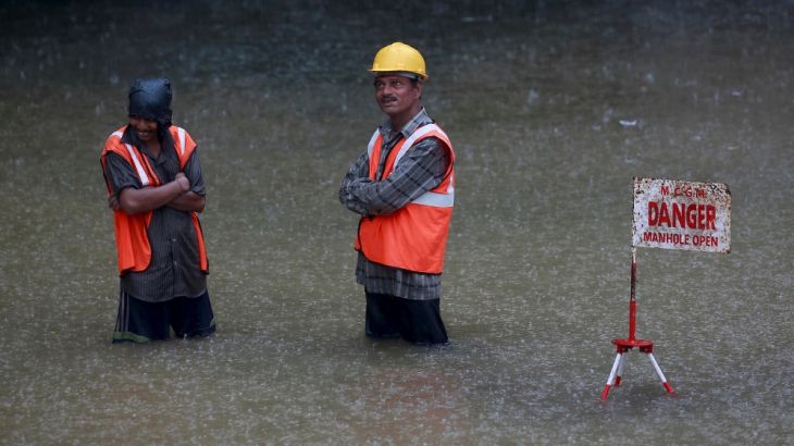 Civic workers stand next to a sign at a flooded road
