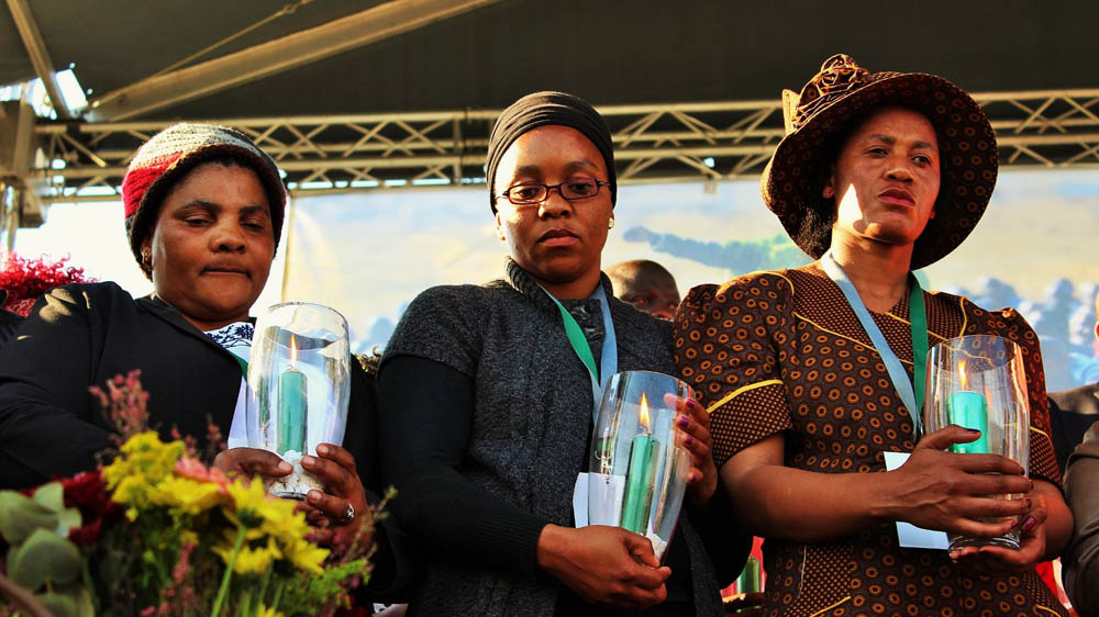 Three Marikana widows hold candles in remembrance of their husbands during commemoration ceremony [Tendai Marima/Al Jazeera]