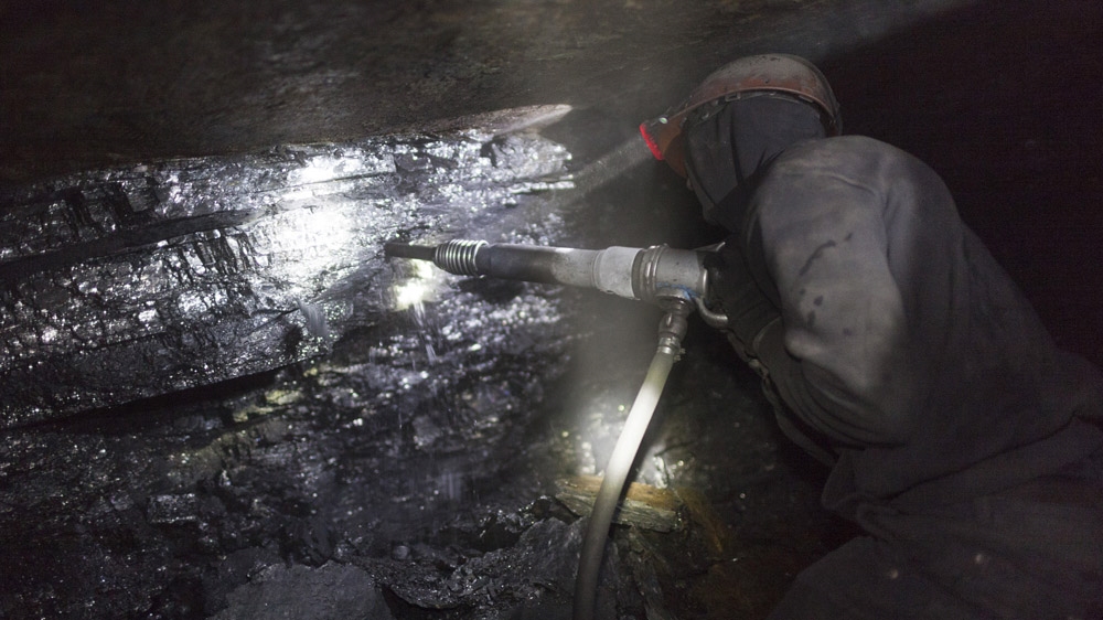 Twenty-three-year-old Tolek works several hundred metres below ground in an illegal mine in Davidovka. His job is to break the coal using a jackhammer, at the deep end of a dark tunnel, which is about half-a-metre in height. [Janos Chiala and Tali Mayer/Al Jazeera]  