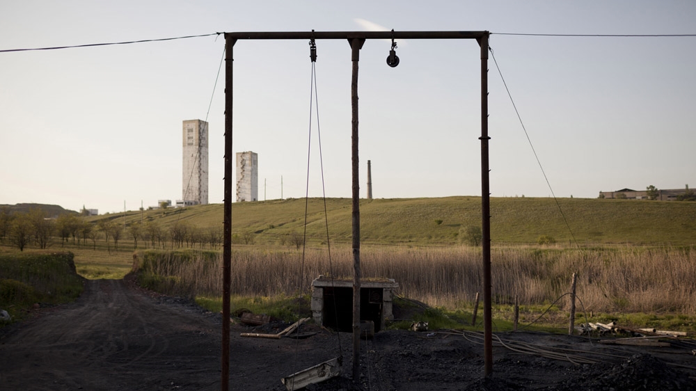 An illegal mine in Davidovka, with the towers of the Glubje mine rising on the horizon. Descending 1,650 metres below the ground, the mine is the deepest in the Donbass. Many miners have died in its tunnels, where temperatures can reach 55 degrees Celsius. [Janos Chiala and Tali Mayer/Al Jazeera]  