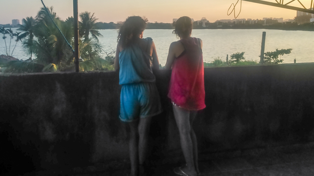 Sandra and her daughter Flora Terra watch the sun set over the lake from Natalia's roof [Maya Thomas-Davis/Al Jazeera]