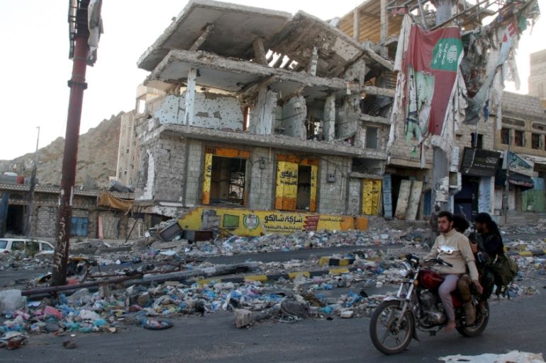 People ride on a motorbike past a building destroyed during recent fighting in Yemen''s southwestern city of Taiz