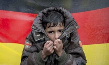 A child tries to warm his hands, backdropped by Germany''s flag
