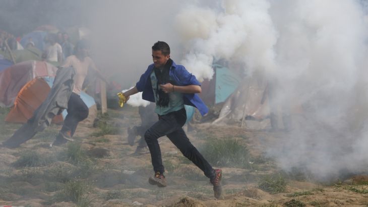 Migrant man runs with a tear gas canister during clashes