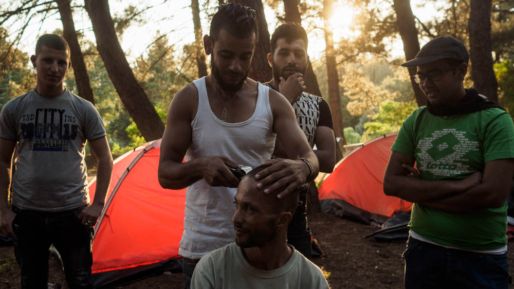 Refugee men kill time by giving haircuts near Evzoni, Greece [Lazar Simeonov/Al Jazeera]