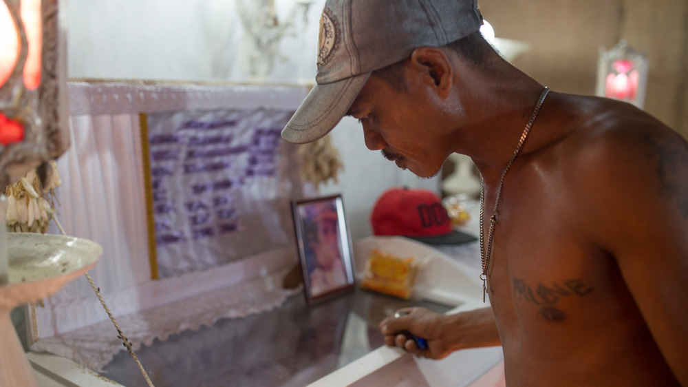 Albert Batiancila, brother of Vicente Batiancila looks at his brother's body through the glass of his casket. Because the family lacked the funds to pay for his burial, they had to hold his wake for 3 weeks to try and gather the funds through donations [Paul Ratje/Al Jazeera]