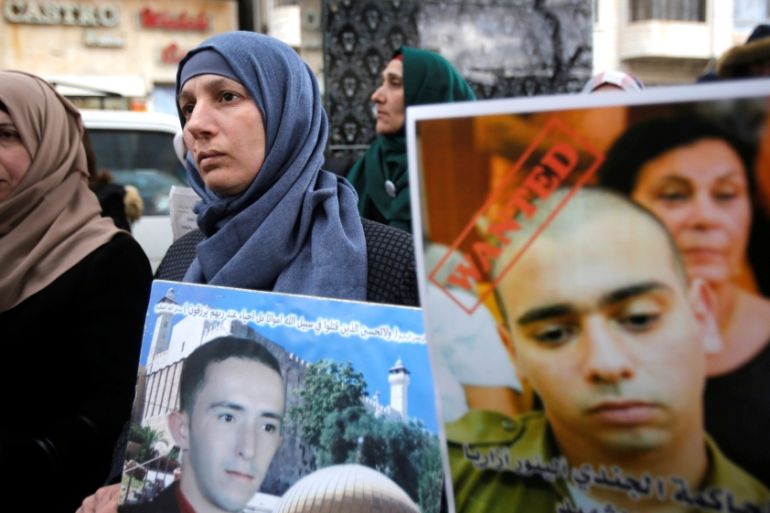 The mother of Palestinian assailant Abdel Fattah al-Sharif holds his poster as another woman holds a poster of Israeli soldier Elor Azaria during a protest in the West Bank city of Hebron