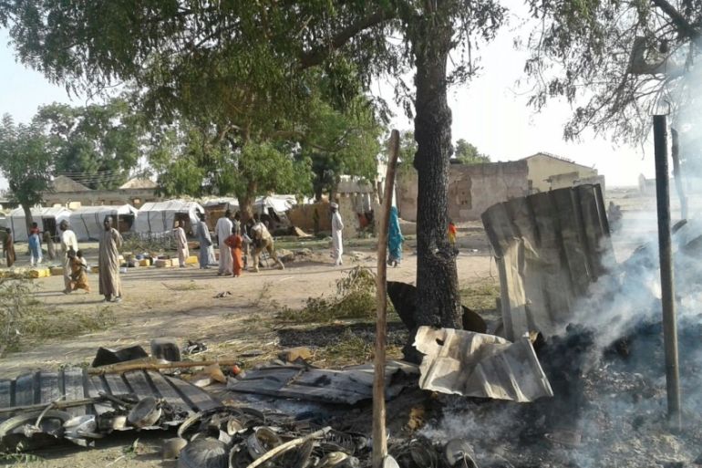 People walk at the site after a bombing attack of an internally displaced persons camp in Rann
