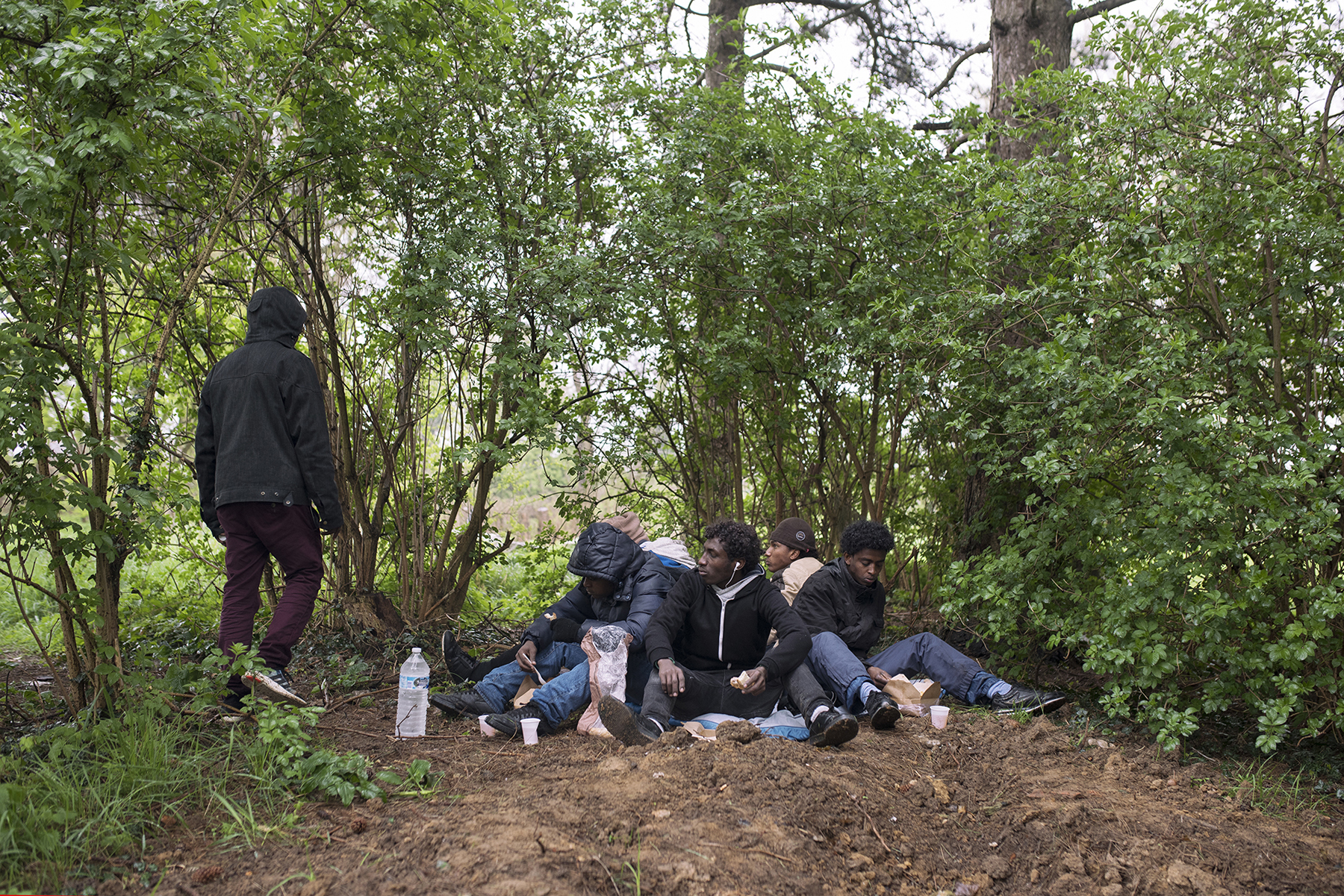 A group of young Eritreans in the forest in Calais eat food from a mobile distribution van operated by the Refugee Community Kitchen [Guillem Trius/Al Jazeera]