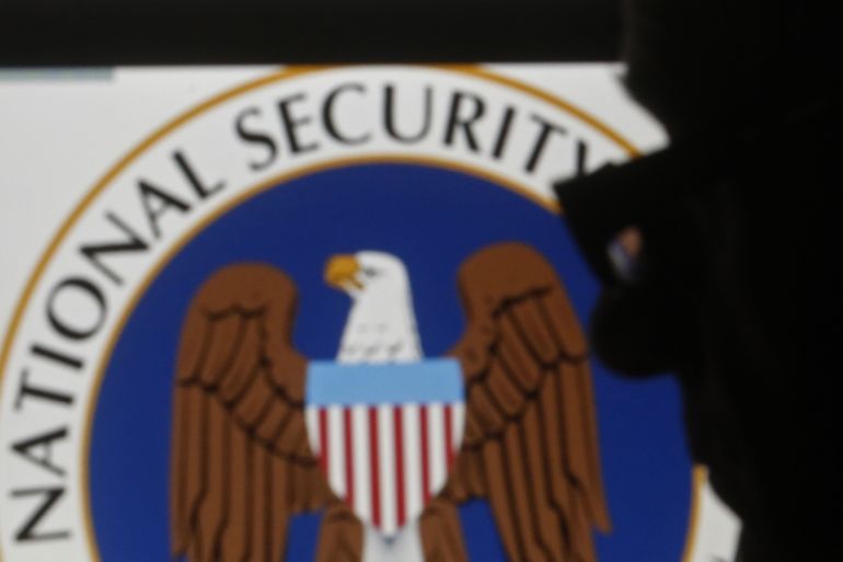 A man is silhouetted near logos of the U.S. National Security Agency (NSA)