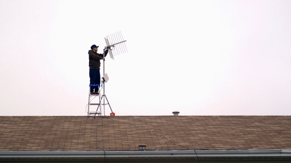 Bruce Buffalo installs one of two antennae for the Maskwacis wifi zone on his sister's roof [Al Jazeera]