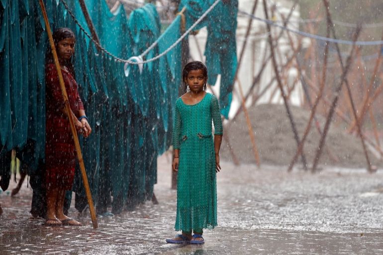 Girls stand in monsoon rains beside an open laundry in New Delhi