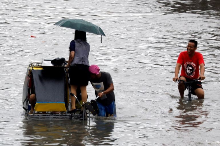 Commuters ride on a pedicab through floodwaters in Las Pinas, Metro Manila