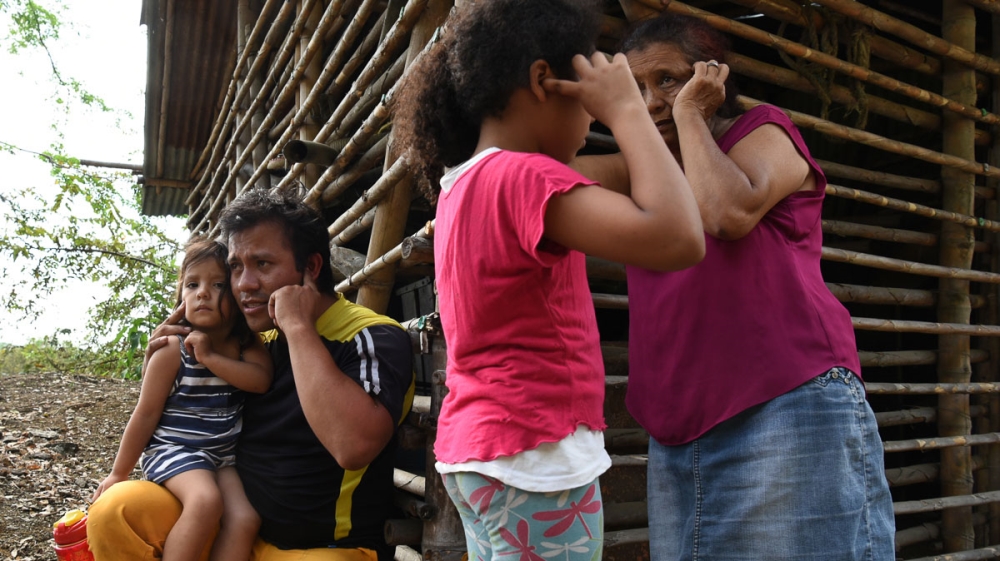 A family covers their ears during controlled explosions in an army operation to deactivate two makeshift bombs placed near a dam at a water treatment plant between El Palo and Toribio [Christian EscobarMora/Mira-V/Al Jazeera]
