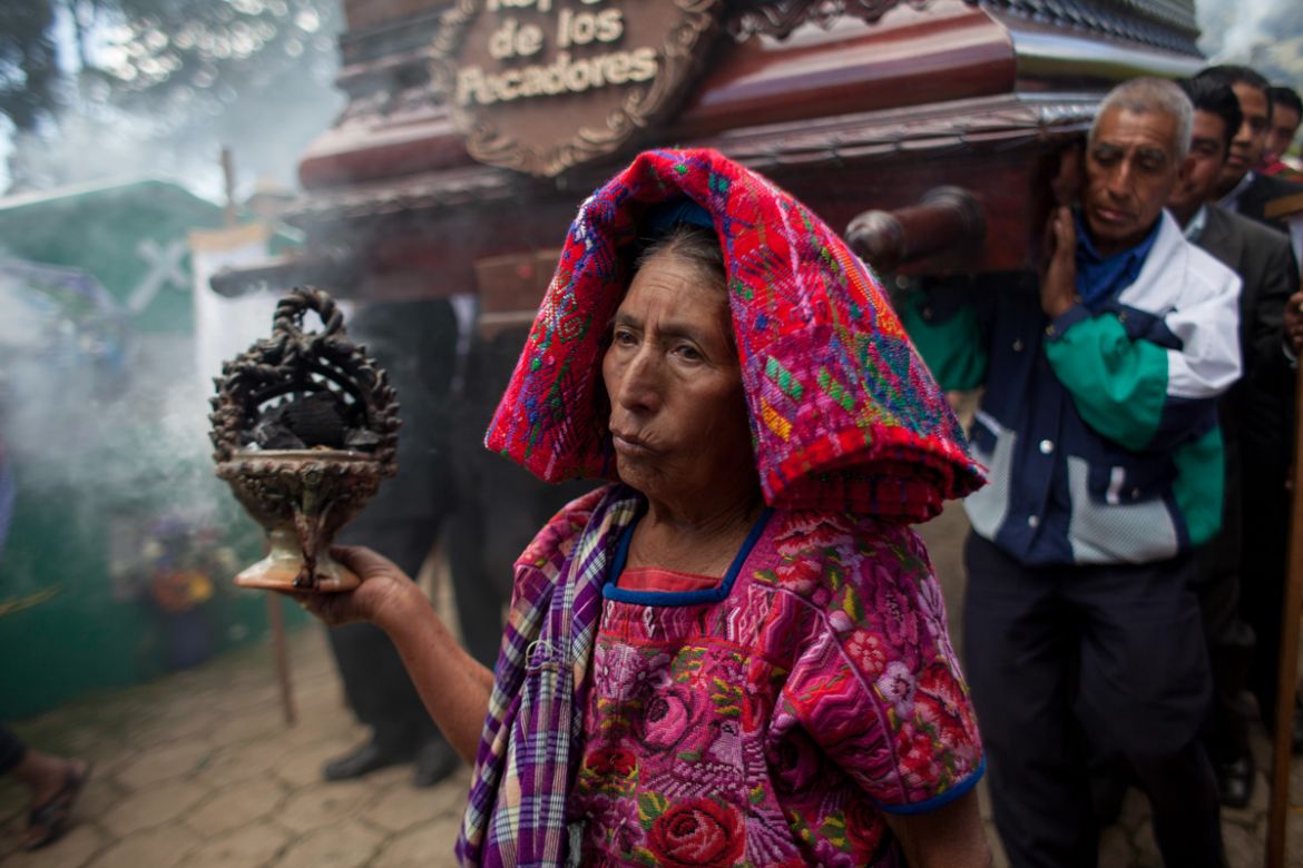 A Kakchiquel Mayan women burns incense as carriers shoulder a religious float with a statue of the Virgin Mary, during Day of the Dead celebrations at the cemetery in Santa Maria de Jesus, Guatemala,