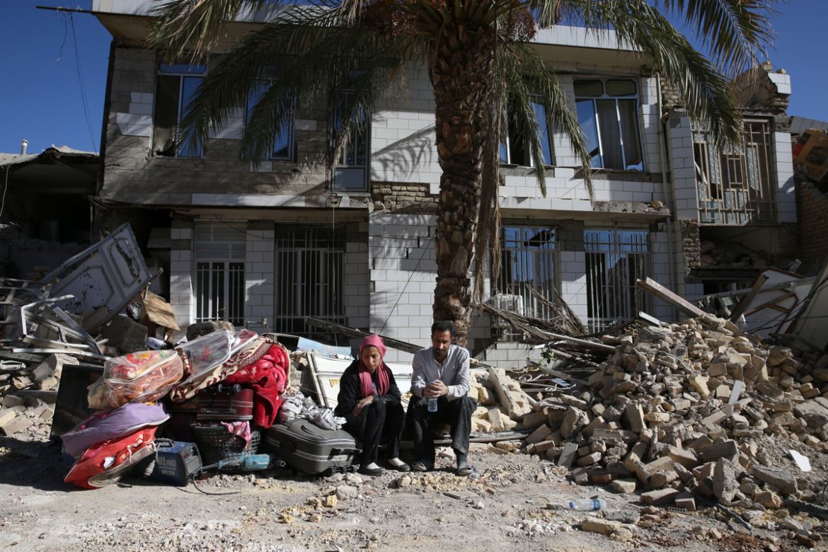 Survivors sit in front of a destroyed house on the earthquake site in Sarpol-e-Zahab in western Iran, Tuesday, Nov. 14, 2017. Rescuers are digging through the debris of buildings felled by the Sunday