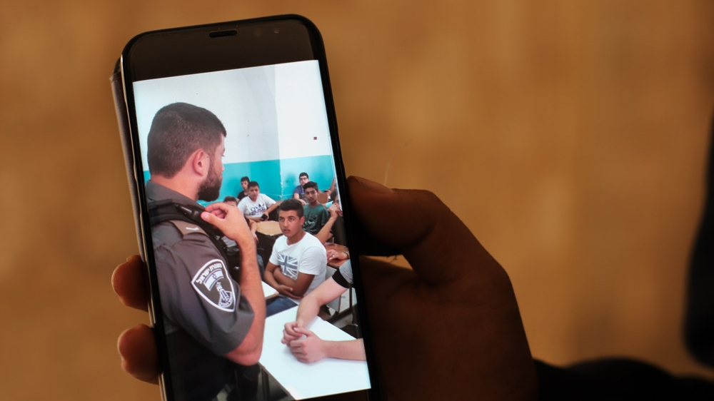 A staff member at Dar al-Aytam shows a picture of a recent Israeli raid on the school [Jaclynn Ashly/Al Jazeera]
