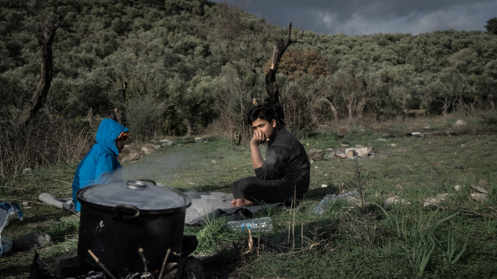 A pair of Afghan boys sit in a field next to the Moria as their family cooks lunch on a campfire [Patrick Strickland/Al Jazeera]
