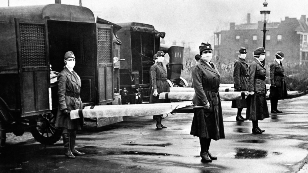 The St Louis Red Cross Motor Corps on duty with mask-wearing women holding stretchers at the backs of ambulances during the Influenza epidemic, St Louis, Missouri, October 1918 [Photo by Underwood Archives/Getty Images]