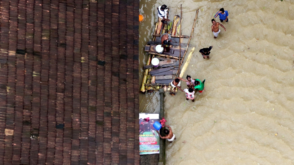 People wait for aid next to a make-shift raft at a flooded area in Kerala state [Sivaram V/Reuters]