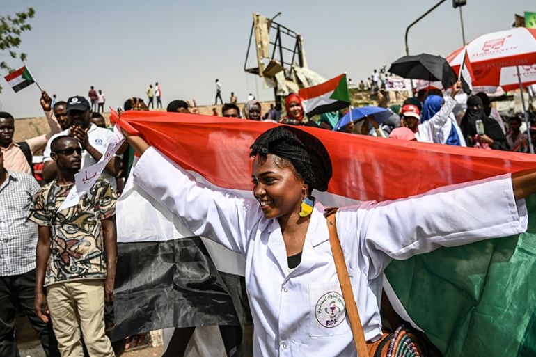 A Sudanese woman walks with a national flag spread behind her as people continue to protest outside the army complex in the capital Khartoum on April 17, 2019. - Sudanese protesters hardened their dem
