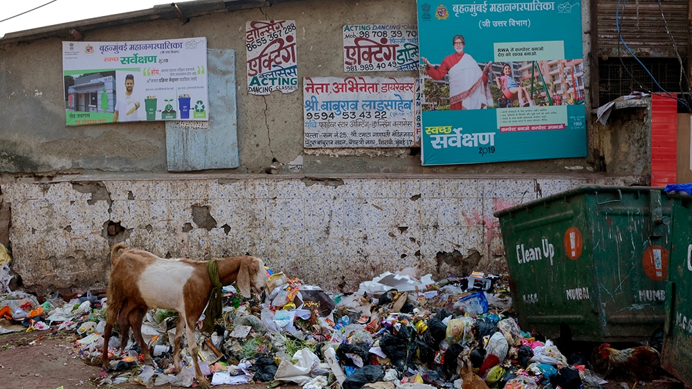 Garbage in the alleys of the slum. Two signs advertise acting classes, and a poster features Bollywood star Amitabh Bachchan [Gayeti Singh/Al Jazeera]