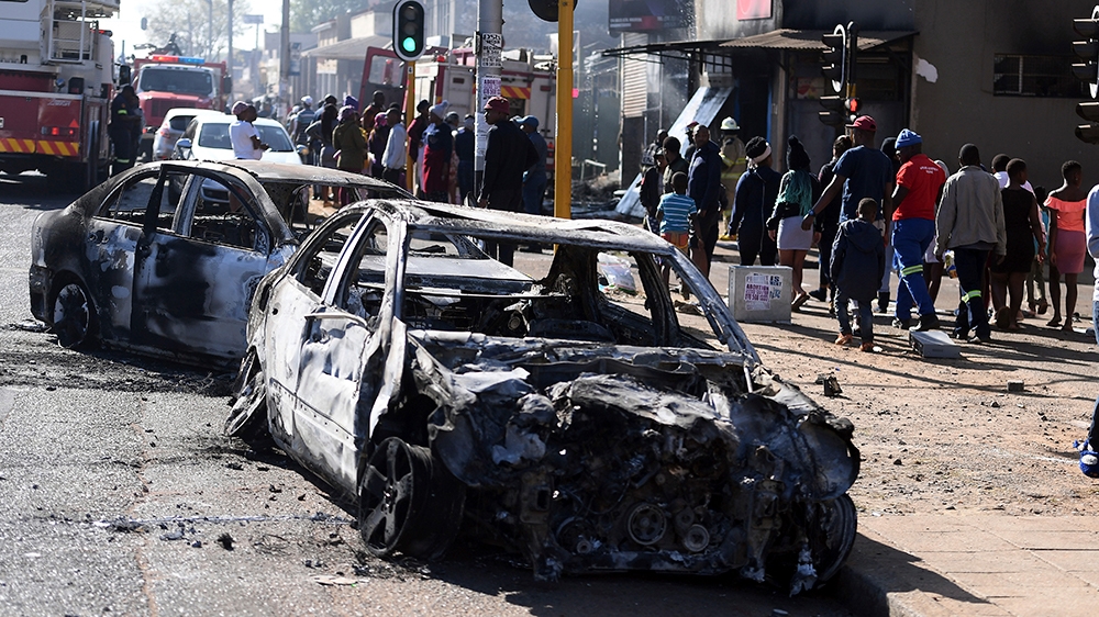 Pedestrians pass burnt out cars on the side of a street on the outskirts of Johannesburg, Monday Sept. 2, 2019. Police had earlier fired rubber bullets as they struggled to stop looters who targeted b